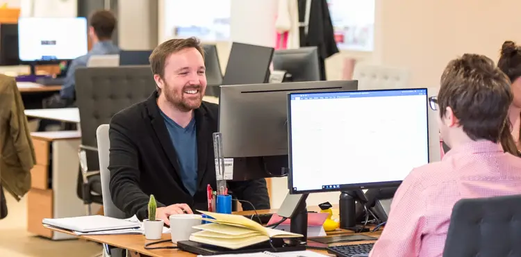 Digital marketing specialists collaborating at desktop computers in a bright, open-plan corporate office.