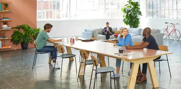 A creative marketing agency team brainstorming and collaborating at a large shared desk in an open-plan office.