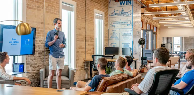 A marketing team lead presenting campaign data during an all-hands strategy meeting in a modern open-plan agency office.