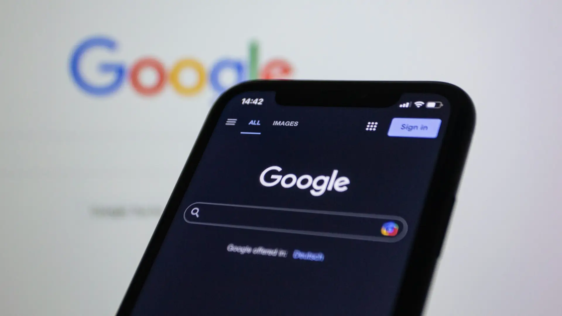 Google landing page on a phone in front of a laptop screen with the google page on too.